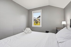 Hotelkamer met een bed, nachtkastje, lamp en raam met uitzicht op een gebouw en bomen.