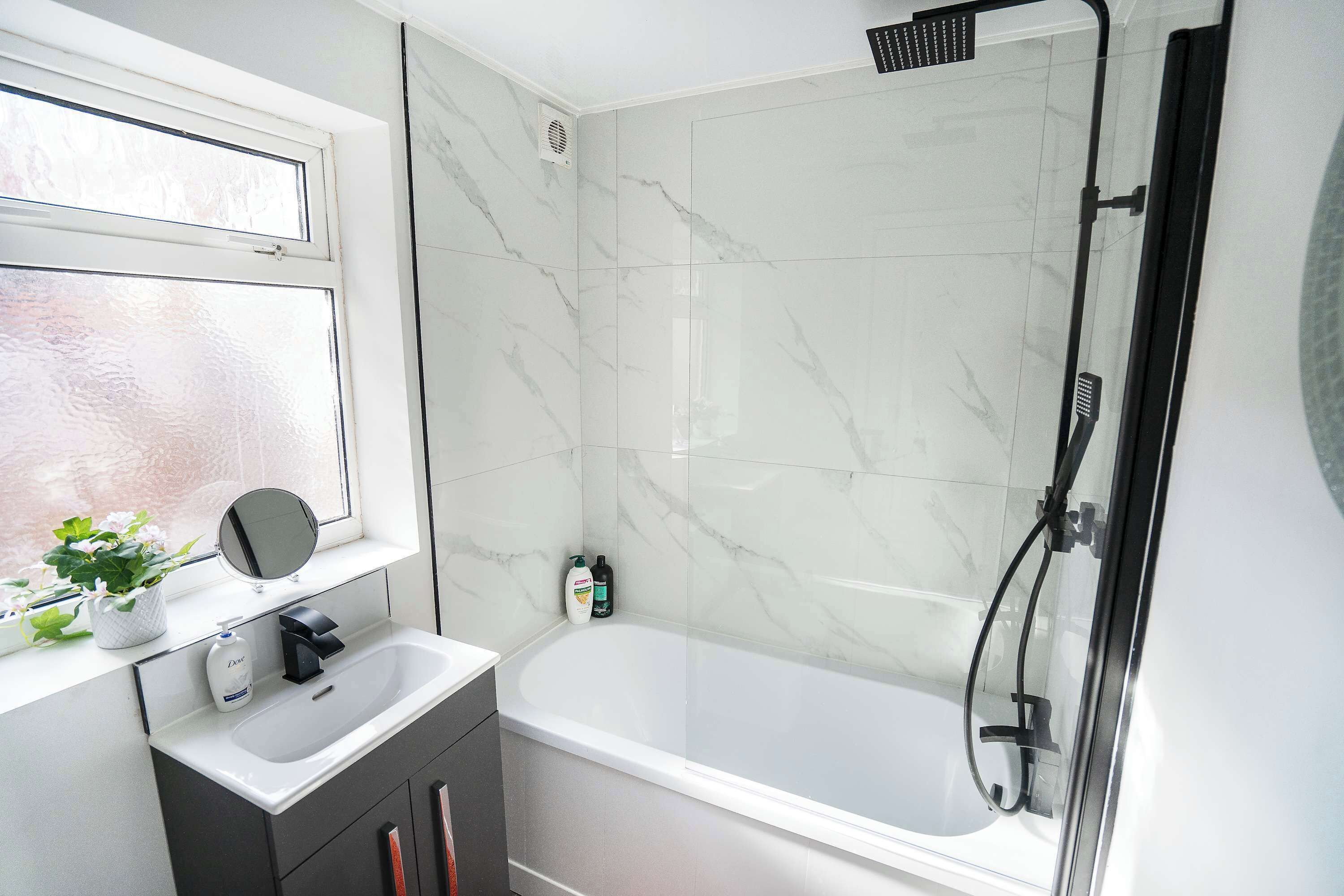 A bathroom with a bathtub, a window with a mirror, and a shower area.