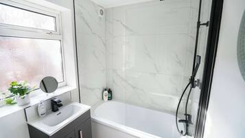 A bathroom with a bathtub, a window with a mirror, and a shower area.
