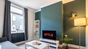 En moderne stue med sofa, sofabord, fjernsyn og reol.