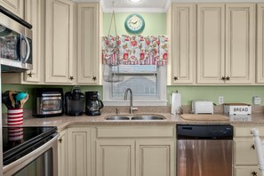 A kitchen with a double sink, stainless steel appliances, and a clock on the wall. - 412 - Oceanfront w/ gorgeous views and open beach (Nags Head)