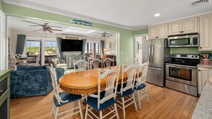 A spacious living room with a wooden dining table, white chairs, and a television. - 412 - Oceanfront w/ gorgeous views and open beach (Nags Head)