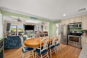 A spacious living room with a wooden dining table, white chairs, and a television. - 412 - Oceanfront w/ gorgeous views and open beach (Nags Head)