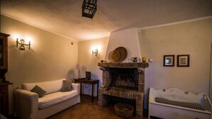 A cozy living room with a fireplace, a sofa, a bench, and wall-mounted lights. - Podere Colombaione - Stalla Apartment (Toscana)