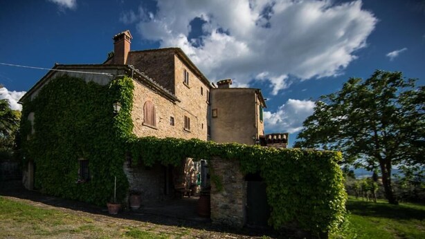 A stone building with ivy-covered walls and a traditional design, featuring a paved entrance and a small garden area. - Podere Colombaione - Stalla Apartment (Toscana)