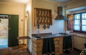 A kitchen with a stone island, wooden hanging rack, and a window with curtains. - Podere Colombaione - Stalla Apartment (Toscana)