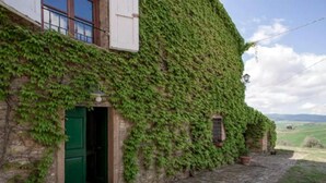 A stone building with a green door, ivy-covered walls, and a view of the countryside. - Podere Colombaione - Stalla Apartment (Toscana)