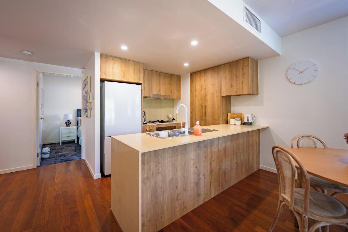 A modern kitchen with wooden cabinets, a central island, and a dining area with a table and chairs.