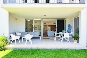 A modern outdoor living area with a sofa, chairs, and a dining table. - Drift South Apartments (Casuarina)