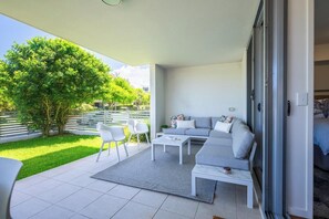 Un espacio exterior moderno con sofá, sillones, una mesa de centro, un árbol y vistas de la vegetación circundante.