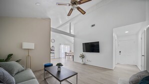 Een moderne woonkamer met een flatscreen televisie, een plafondventilator en een eethoek met een tafel en stoelen.