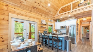 A wooden interior with a dining area, kitchen, and a view of the outdoors. - New Luxury Smoky Mountain Cabin, Hot Tub, Fire Pit, Mountain Views & Easy Access (SEVIERVILLE)