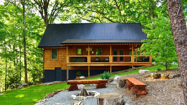 A log cabin with a deck, surrounded by a forest. - New Luxury Smoky Mountain Cabin, Hot Tub, Fire Pit, Mountain Views & Easy Access (SEVIERVILLE)