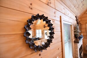 Ein Holzinnenraum mit einem runden Spiegel an der Wand, einem Kamin mit einem kleinen Baum und einem Essbereich, der durch ein Fenster sichtbar ist.