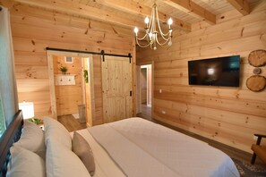 Ein Zimmer mit Holzwandverkleidung, einem Bett, einer Kristallleuchtreiter, einem Flachbildfernseher und einer Schiebetür zu einem anderen Raum.