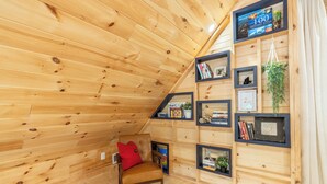 A cozy attic room with wooden walls, a leather chair, and a bookshelf filled with books and framed photos. - New Luxury Smoky Mountain Cabin, Hot Tub, Fire Pit, Mountain Views & Easy Access (SEVIERVILLE)