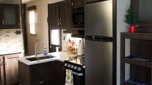 Una cocina compacta con muebles de madera oscura, un refrigerador de acero inoxidable, un microondas y una estufa.