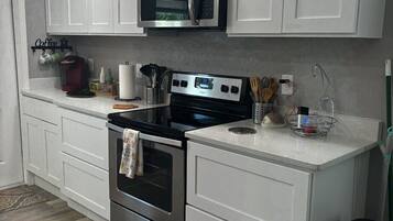 A modern kitchen with white cabinetry, stainless steel appliances, and a coffee station.