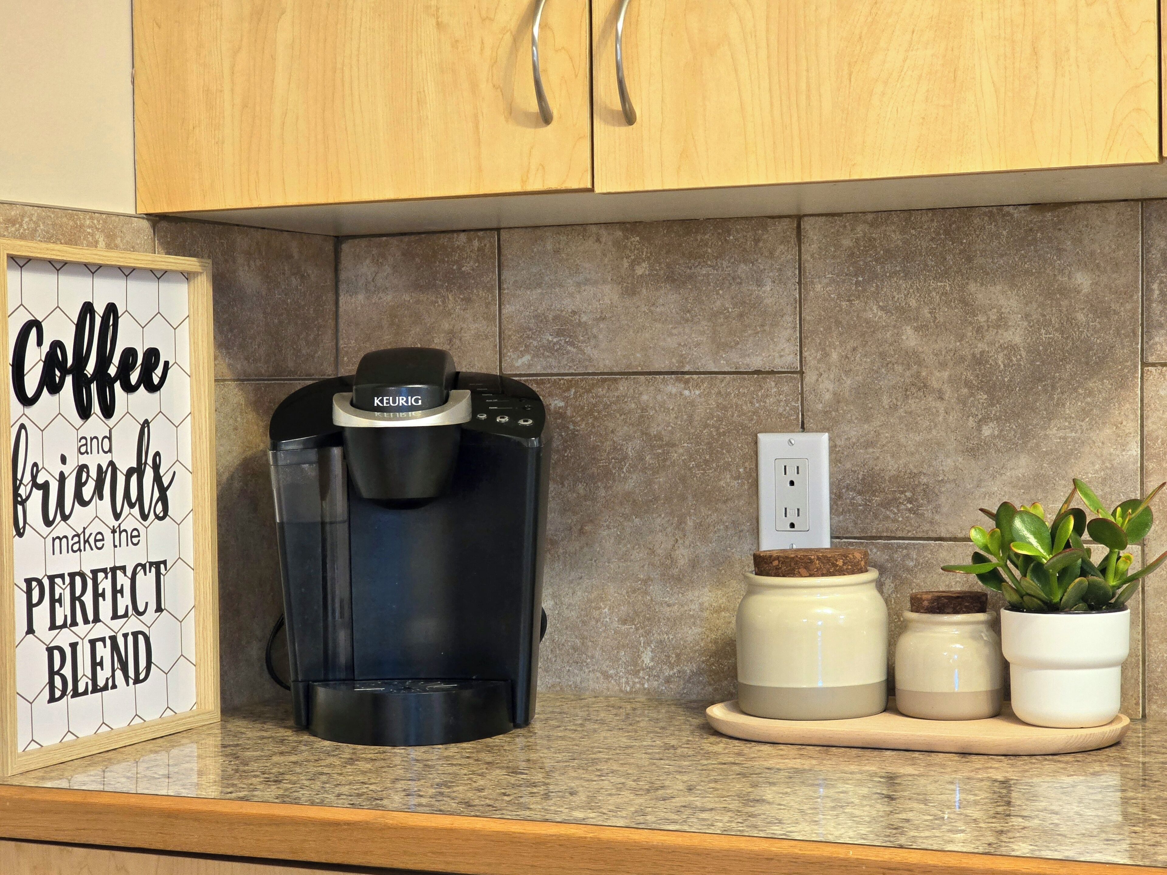 A coffee maker on a countertop with a sign that reads 'Coffee and friends make the perfect blend.'