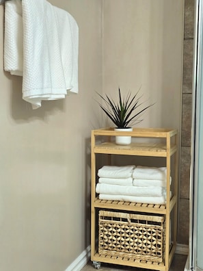 Ein Badezimmer mit einem hölzernen Regal, auf dem Handtücher und ein Topfpflanze stehen.