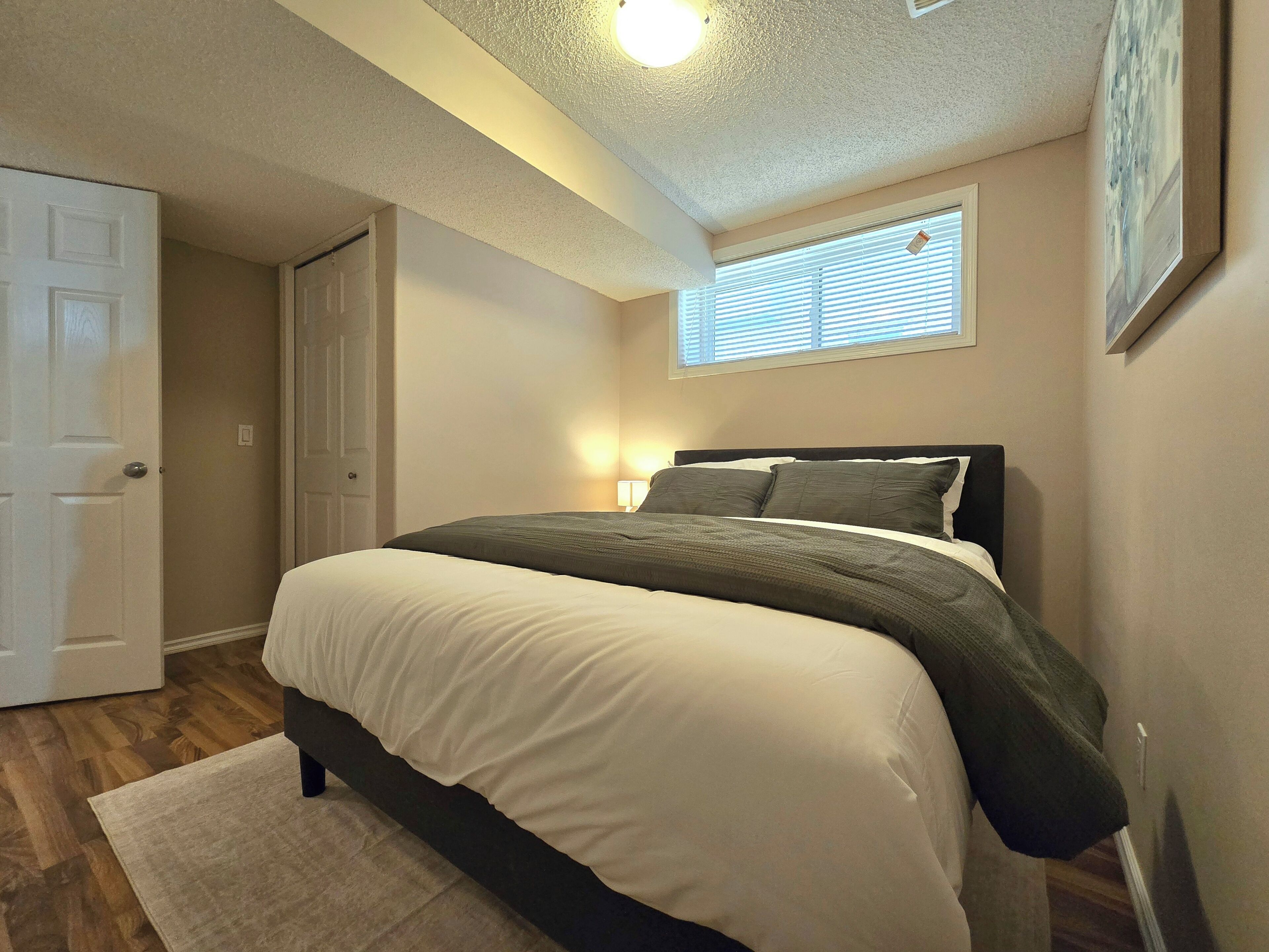 A bedroom with a bed, a nightstand, a window with blinds, and a door.