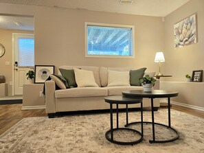 Ein Wohnzimmer mit einem beigen Sofa, einem runden Couchtisch, einer Topfpflanze, einer Wandlampe und einem gerahmten Bild.