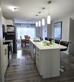 A modern kitchen with a central island, a dining area with chairs, a refrigerator, and a sink. - Comfy + Spacious 3 BR Home on the park, in strategic SW of Edmonton/near airport (Edmonton)