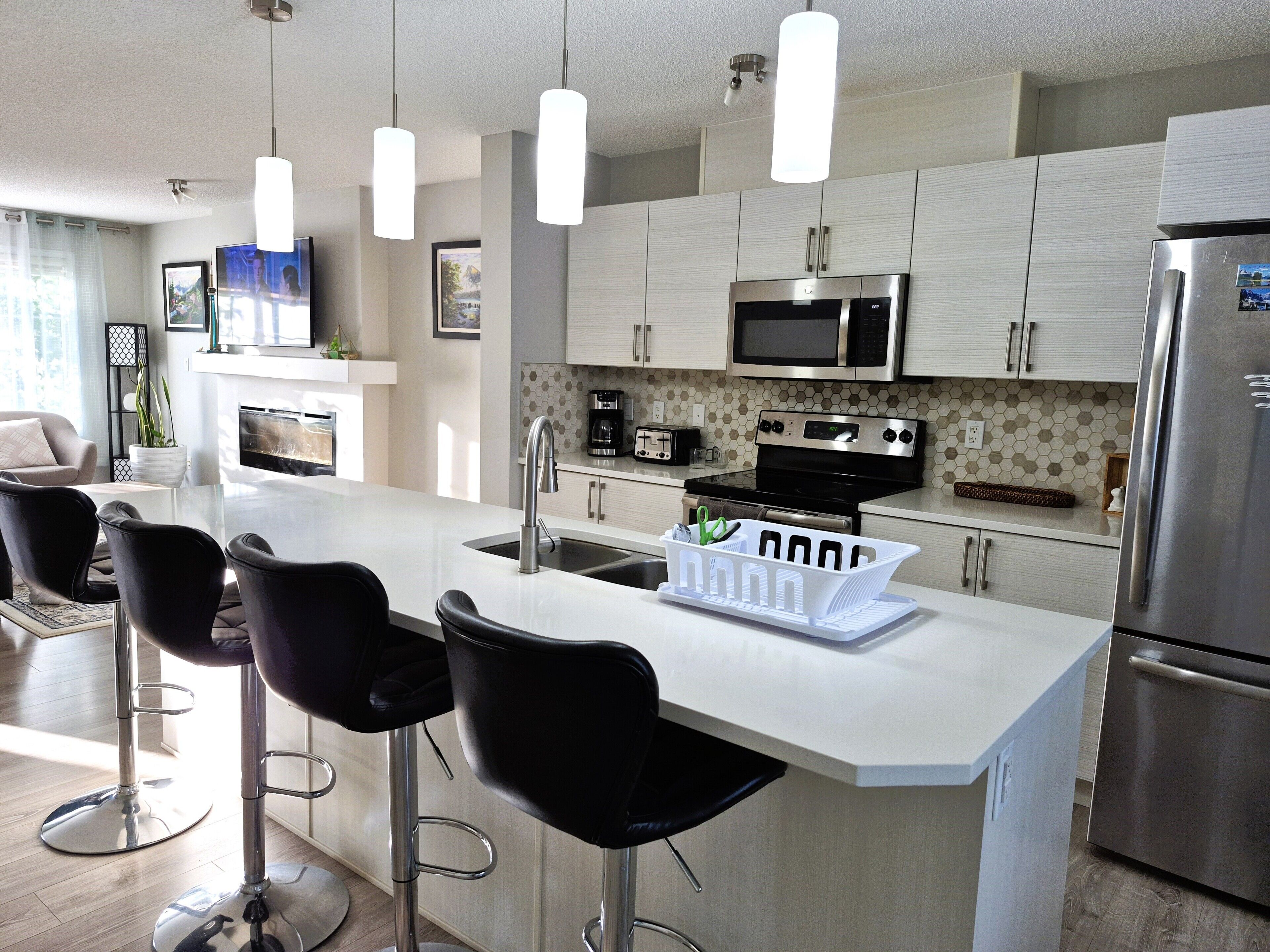 A modern kitchen with a central island, bar stools, stainless steel appliances, and pendant lighting.