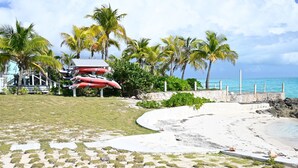 Una playa con arena blanca, palmeras y un edificio con canoas rojas.