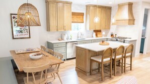 Une cuisine moderne avec des meubles en bois, un îlot central doté de tabourets de bar, une table à manger avec des chaises et des luminaires suspendus.