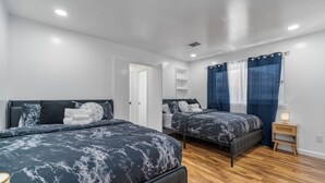 Un dormitorio con dos camas, suelo de madera, una mesita de noche y una puerta que da a otra habitación.