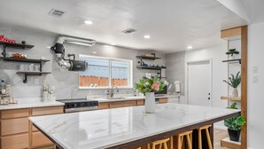 Una cocina moderna con encimera de mármol, taburetes de madera y electrodomésticos integrados.