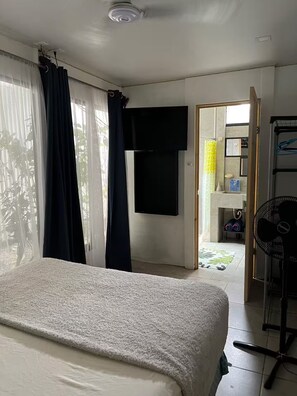 A bedroom with a bed, a TV, a fan, and a bathroom visible through an open door. - Entire Downtown Home with Private Pool & A/C (Uvita)