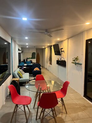 A modern living room with a glass table, red chairs, a sofa, and a ceiling fan. - Entire Downtown Home with Private Pool & A/C (Uvita)