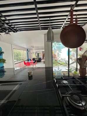 A modern kitchen with a gas stove, hanging pot rack, and a dining area with a round table and chairs. - Entire Downtown Home with Private Pool & A/C (Uvita)