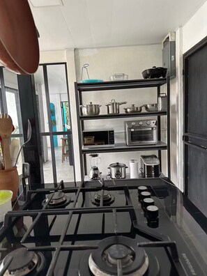 A kitchen with a gas stove, a microwave, a toaster, and a shelf with pots and pans. - Entire Downtown Home with Private Pool & A/C (Uvita)