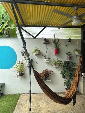 A hammock under a corrugated metal roof, with potted plants on shelves and a blue circle on the wall. - Entire Downtown Home with Private Pool & A/C (Uvita)