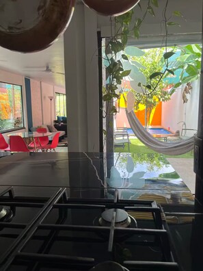A modern kitchen with a large window, red chairs, and a hammock outside. - Entire Downtown Home with Private Pool & A/C (Uvita)