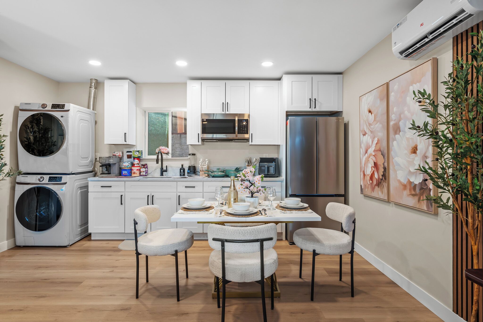 Una cocina moderna con armarios blancos, electrodomésticos de acero inoxidable y un comedor con una mesa dispuesta para cuatro.