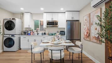 Una cocina moderna con armarios blancos, electrodomésticos de acero inoxidable y un comedor con una mesa dispuesta para cuatro.