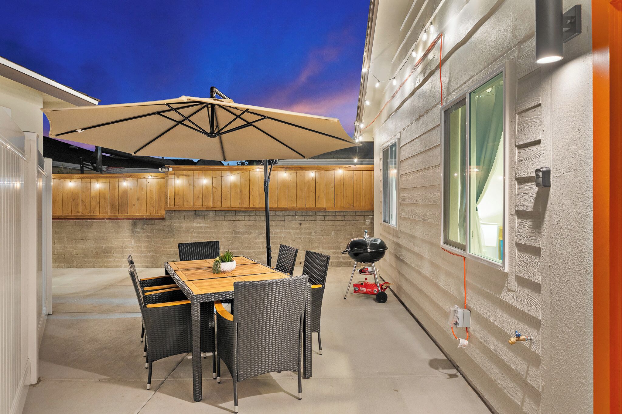 Eine Terrasse im Freien mit Tisch, Stühlen, einem Grill und Lichterketten.