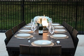 A rectangular outdoor dining table set for six with a bottle of wine, glasses, and plates. - Private Oasis with Luxury Heated Pool, Hot Tub & 100" TV (Clive)