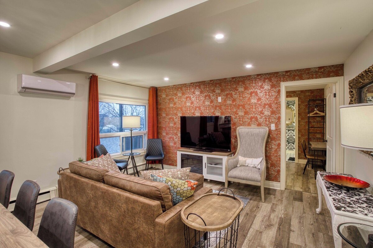 A living room with a sofa, chairs, a television, and a dining area with a table and chairs.