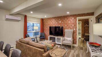 A living room with a sofa, chairs, a television, and a dining area with a table and chairs.