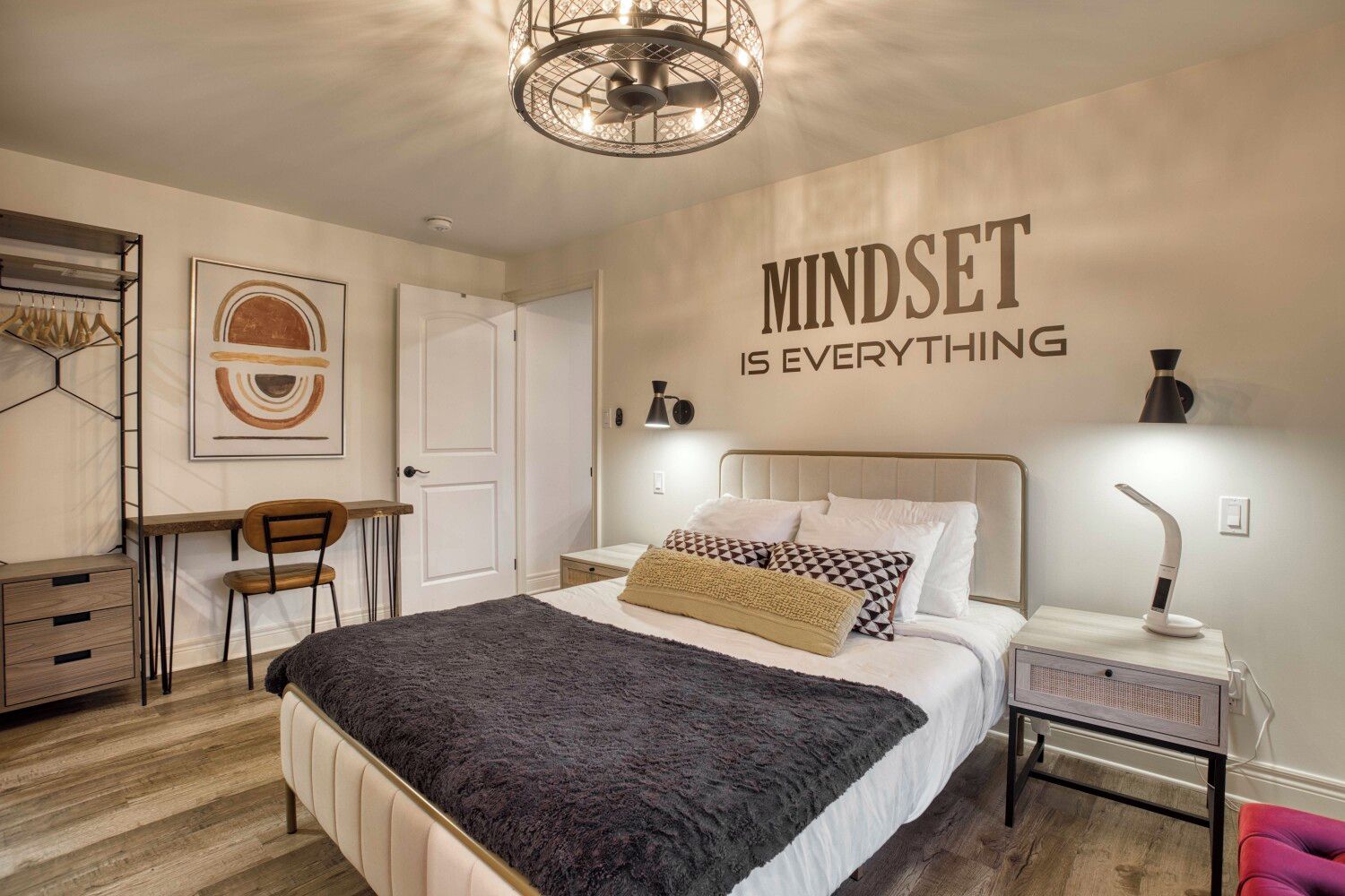 A bedroom with a bed, bedside table, lamp, and a motivational quote on the wall.