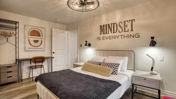 A bedroom with a bed, bedside table, lamp, and a motivational quote on the wall.