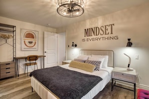 Un dormitorio con cama, mesita de noche, lámpara y una frase motivadora en la pared.