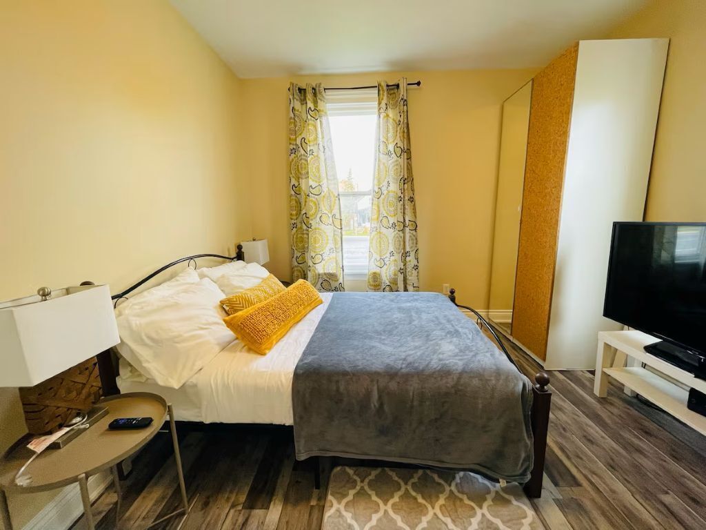 Una habitación de hotel con cama, televisión, escritorio con lámpara y ventana con cortinas.