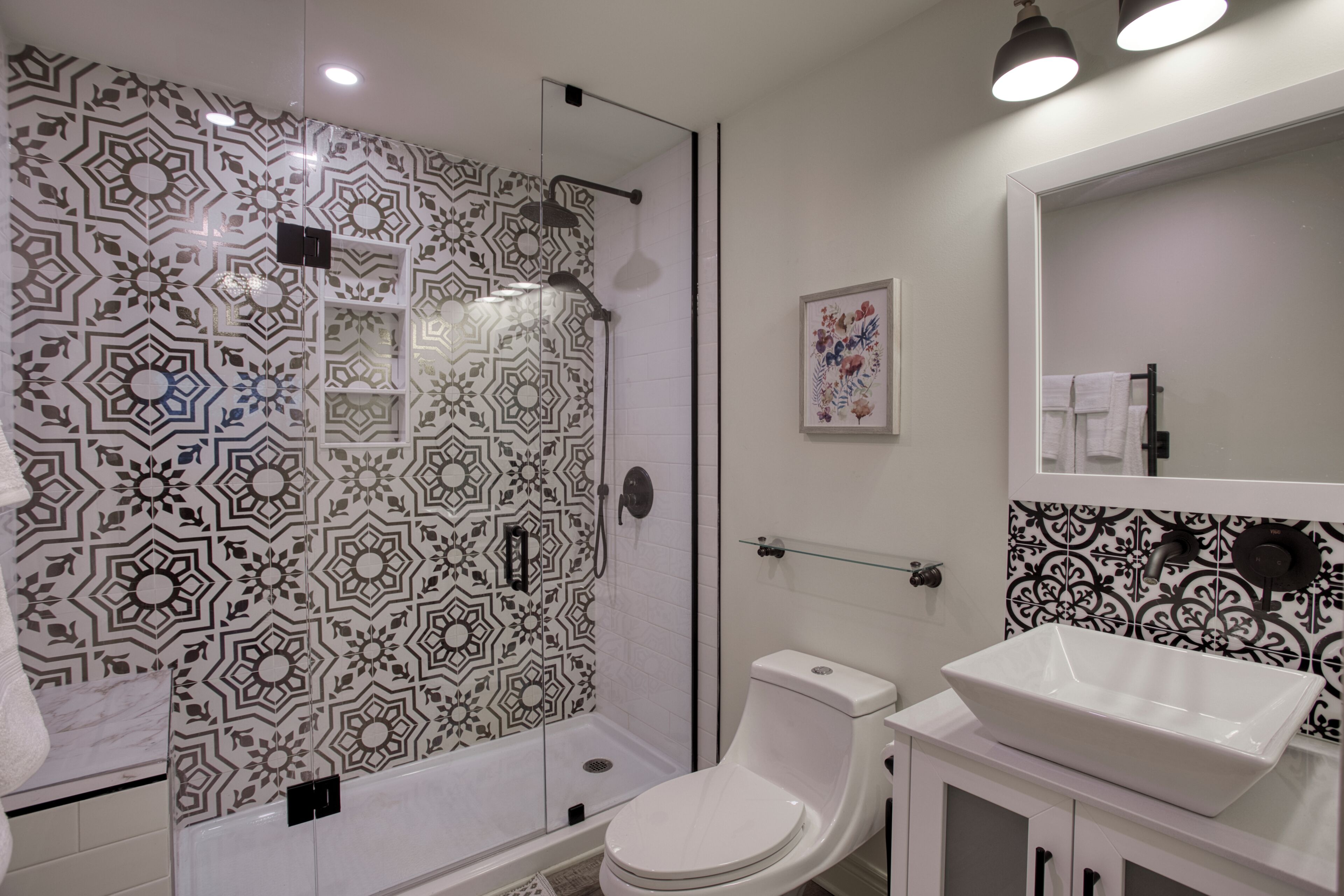 A bathroom with a patterned shower wall, a toilet, a sink, and a mirror.