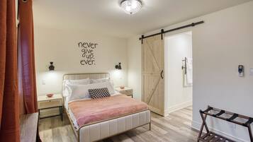 Un dormitorio con cama, lámpara fijada a la pared, puerta corredera estilo granero y una cita inspiradora en la pared.
